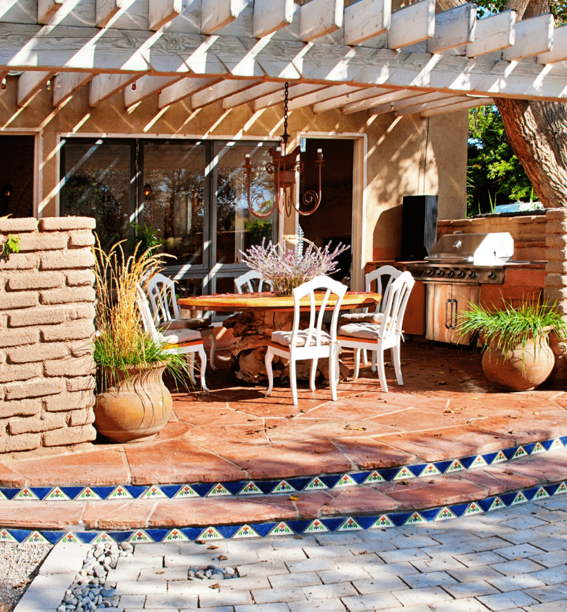 An outdoor kitchen and dining area with a brick wall backdrop and a white pergola overhead